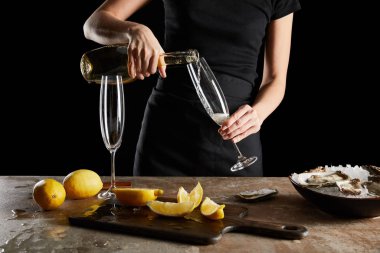 Şampanya bardağına köpüklü şarap döken bir kadın. İstiridye ve limonların yanında. Siyah üzerine izole edilmiş. 