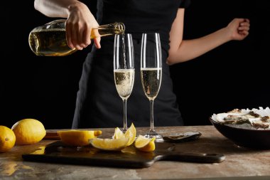 cropped view of woman pouring sparkling wine in champagne glass near oysters in bowl with ice isolated on black  clipart