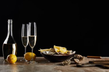 İstiridyelerin yanında köpüklü şarap ve siyah kasede limonlu şampanya bardakları. 