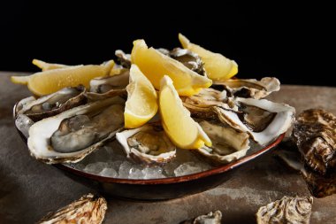 close up of oysters and lemons in bowl with ice isolated on black  clipart