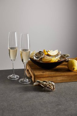 oysters and fresh lemons in bowl near champagne glasses with sparkling wine isolated on grey  clipart