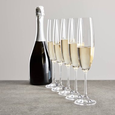 selective focus of champagne glasses with sparkling wine near bottle isolated on grey  clipart