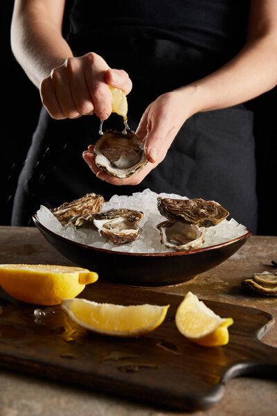 selective focus of woman squeezing lemon on oyster isolated on black 