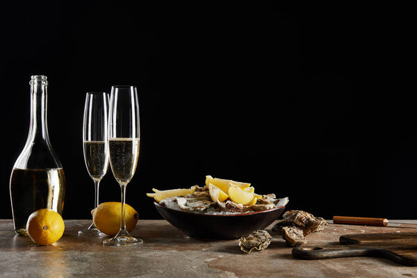 champagne glasses with sparkling wine near oysters and lemons in bowl isolated on black 