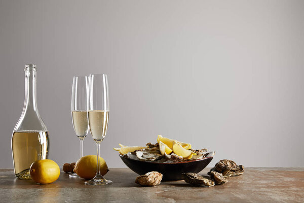 champagne glasses with sparkling wine near oysters and lemons in bowl isolated on grey 