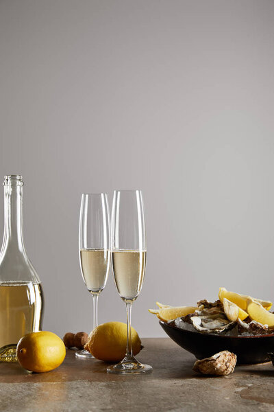 champagne glasses with sparkling wine near bottle, oysters and lemons in bowl isolated on grey 