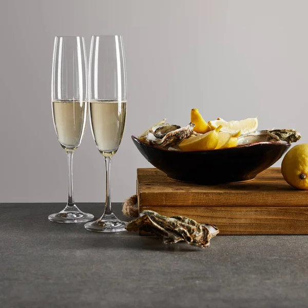 シャンパングラスのそばのボウルに新鮮な牡蠣とレモンとグレーに輝くワイン — ストック写真
