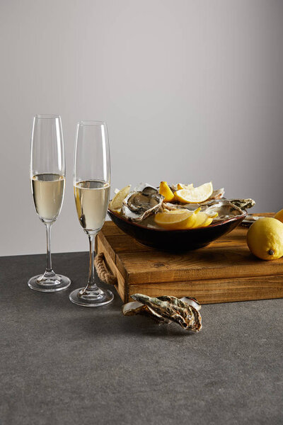 oysters and fresh lemons in bowl near champagne glasses with sparkling wine isolated on grey 