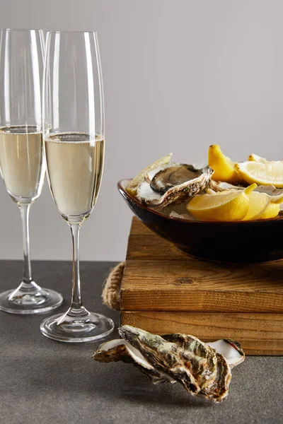 选择重点的牡蛎和新鲜柠檬放在香槟酒杯附近的碗中 用灰色隔热的闪闪发光的葡萄酒 — 图库照片