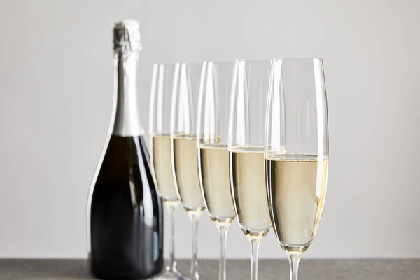 selective focus of sparkling wine in champagne glasses near bottle isolated on grey 