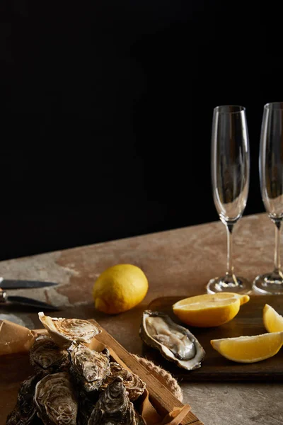 选择性地将牡蛎集中在木制切菜板上柠檬附近的贝壳中 并将香槟酒杯与黑色隔离 — 图库照片