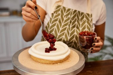 Cropped view of confectioner putting berry jam on cake clipart