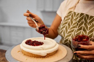 Cropped view of confectioner adding tasty berry jam on cake clipart