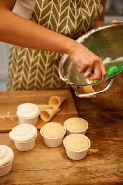 Cropped view of confectioner mixing cream for cupcakes and waffle cones on table clipart