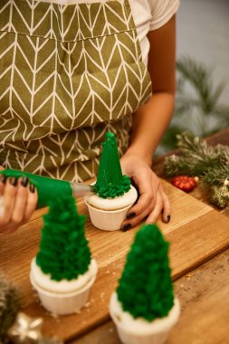 Noel ağacı kekleri süsleyen şekerci manzaralı ladin dalları ve masa üstünde noel baloları.