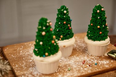 Selective focus of Christmas tree cupcakes with flour and christmas ball on cutting board clipart