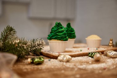 Masada yeşil kremalı, Noel topları ve masa üzerinde çam dalı olan lezzetli kekler.