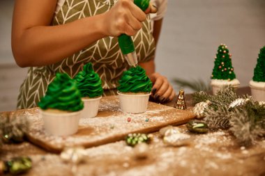 Noel ağacı kekleri süsleyen şekerci manzarası. Noel balolarının yanında krema ve masa üstünde çam dalları.