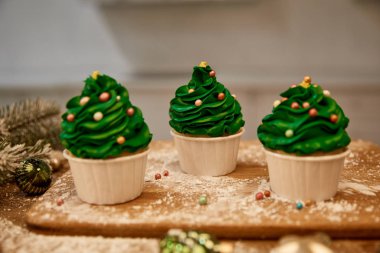 Yeşil kremalı kekler ve masasında ladin dalı olan noel baloları.