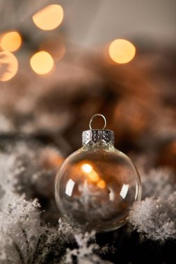 Karda ladin dallarında şeffaf noel balosu, bulanık sarı ışıklarla.