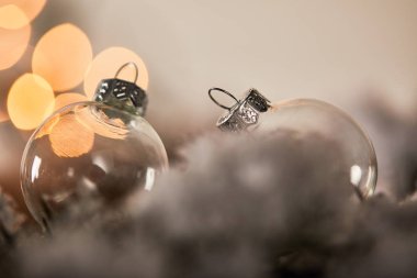 Karda ladin dallarında saydam noel baloları ve sarı ışıklar.
