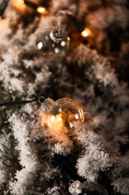 Şeffaf noel balolarının seçici odağı ve kardaki ladin dallarının üzerindeki sarı ışıklar
