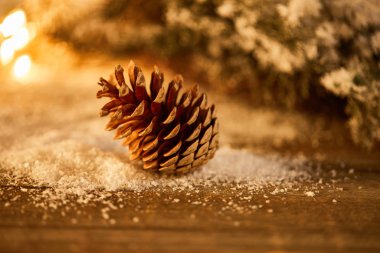 Karda ladin dalları ve bulanık noel ışıkları olan ahşap masa üzerindeki dekoratif çam kozalağı.