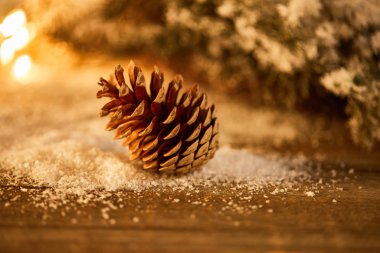 decorative pine cone on wooden table with spruce branches in snow and blurred christmas lights clipart