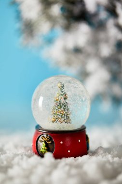 Kartopu içindeki dekoratif Noel ağacı kar ve ladin dallarıyla maviliğin üzerinde duruyor.