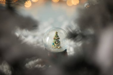Küçük kartopunun seçici odak noktası. Karda duran noel ağacı. Dalları ve ışıkları bokeh. 