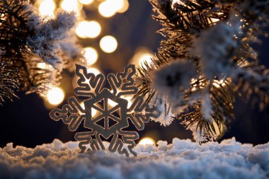 Karda ladin dalları ve bulanık noel ışıkları olan dekoratif kar tanelerine yakın durun. 