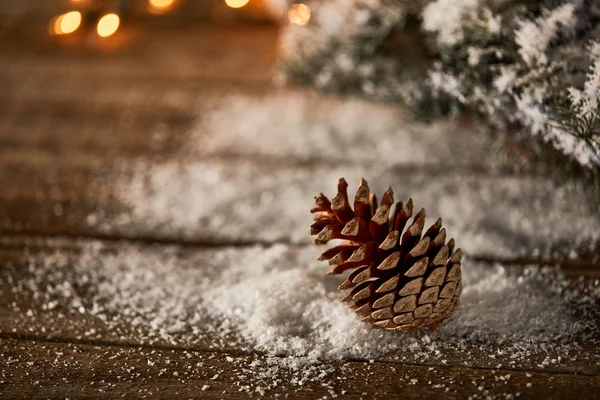 Tannenzapfen Auf Holztisch Mit Fichtenzweigen Schnee Und Verschwommener Weihnachtsbeleuchtung — Stockfoto