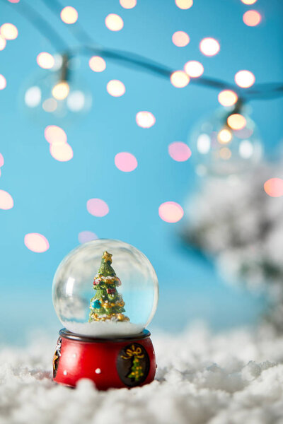 christmas tree in snowball standing on blue with snow and blurred lights