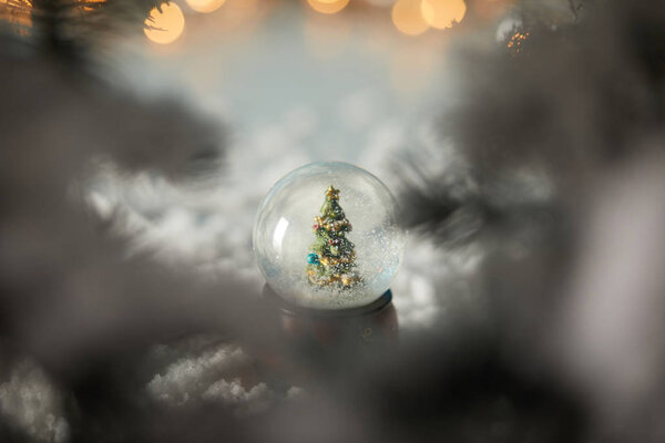селективный фокус маленького снежка с рождественской елкой, стоящей в снегу с еловыми ветвями и огнями боке
 