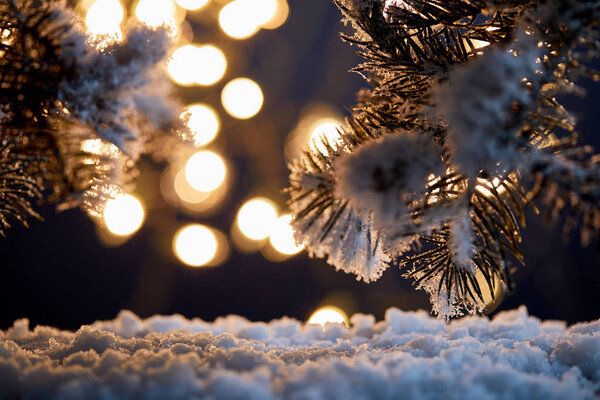 close up of spruce branches in snow with christmas lights bokeh at night  