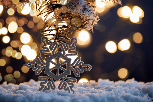 decorative snowflake with spruce branches in snow with christmas lights bokeh 