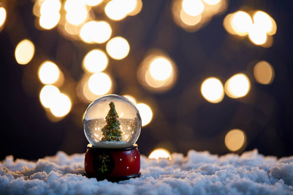 christmas tree in snowball standing in snow with blurred lights at night