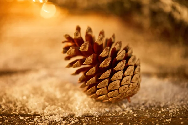 One pine cone on wooden table in snow and christmas lights bokeh — Stock Image One Pine Cone Wooden Table Snow Christmas Lights Bokeh Stock Image