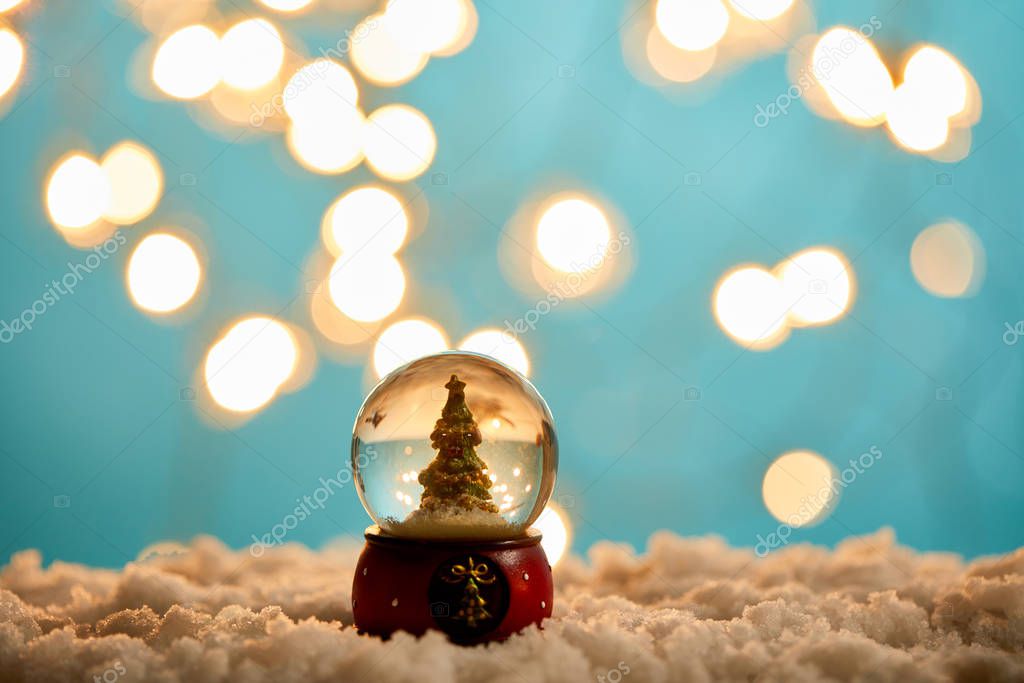 little christmas tree in snowball standing on blue with snow and blurred lights 