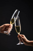 abgeschnittene Ansicht eines Paares, das mit Champagnergläsern klingelt und Heiligabend feiert, isoliert auf schwarz