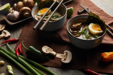 Kavanozlu geleneksel baharatlı ramen ve taş yüzeyde kahverengi peçete üzerine sebze.