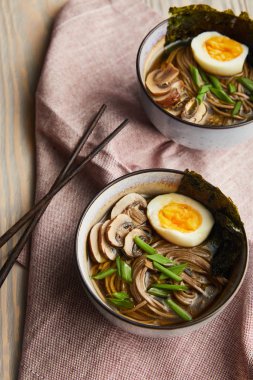 Geleneksel baharatlı ramen tabakta, yemek çubuklarıyla ahşap masada peçeteyle