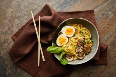 Tabaktaki geleneksel baharatlı ramen ve taş yüzeyde kahverengi peçeteli yemek çubukları.