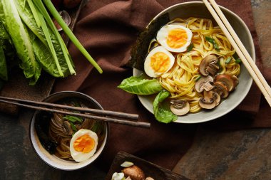 Geleneksel baharatlı ramen tabakta, kahverengi peçeteyle taş yüzeyde yemek çubukları.