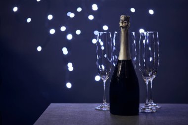 Bir şişe şampanya ve bulanık Noel ışıkları olan bardaklar. 