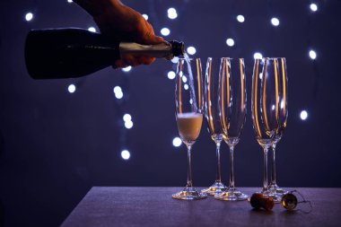 cropped view of man pouring sparkling wine into glasses with christmas lights bokeh clipart