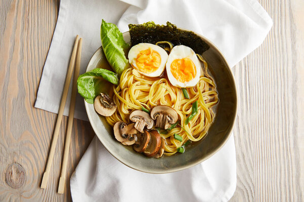 top view of traditional asian ramen in bowl near chopsticks on napkin on wooden table