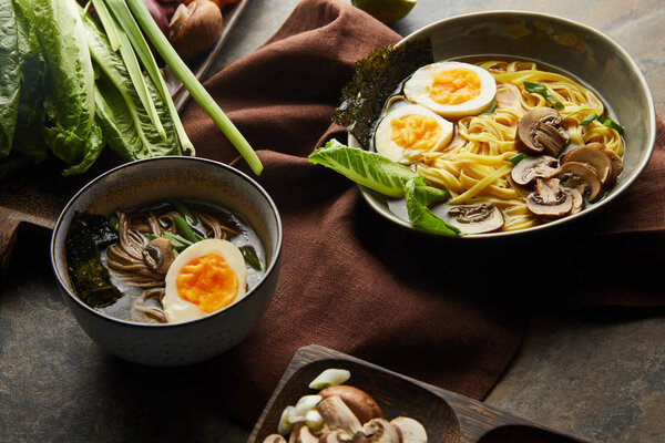 traditional spicy ramen in bowls with chopsticks on brown napkin on stone surface