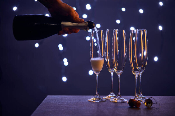 cropped view of man pouring sparkling wine into glasses with christmas lights bokeh