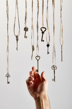 cropped view of man touching vintage keys hanging on ropes isolated on white clipart